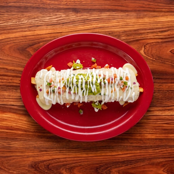 A large burrito topped with white sauce, guacamole, and pico de gallo on a red plate.