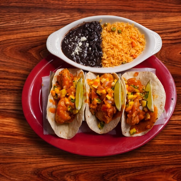 Three shrimp tacos with mango salsa and lime wedges, served with rice and black beans.