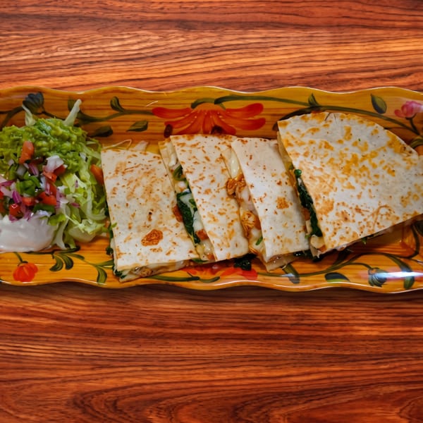 Quesadillas with guacamole, pico de gallo, and sour cream on a decorative plate.