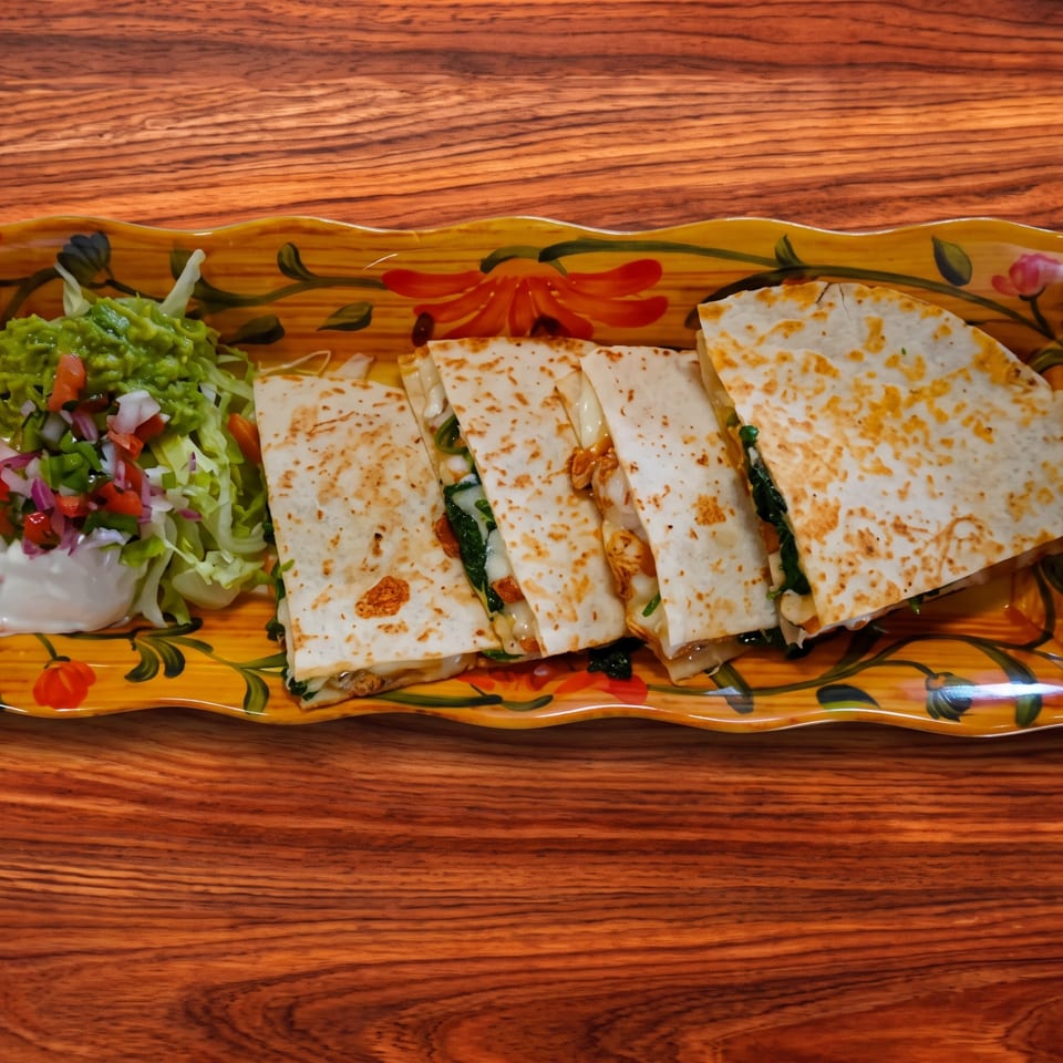 Quesadillas with guacamole, pico de gallo, and sour cream on a decorative plate.